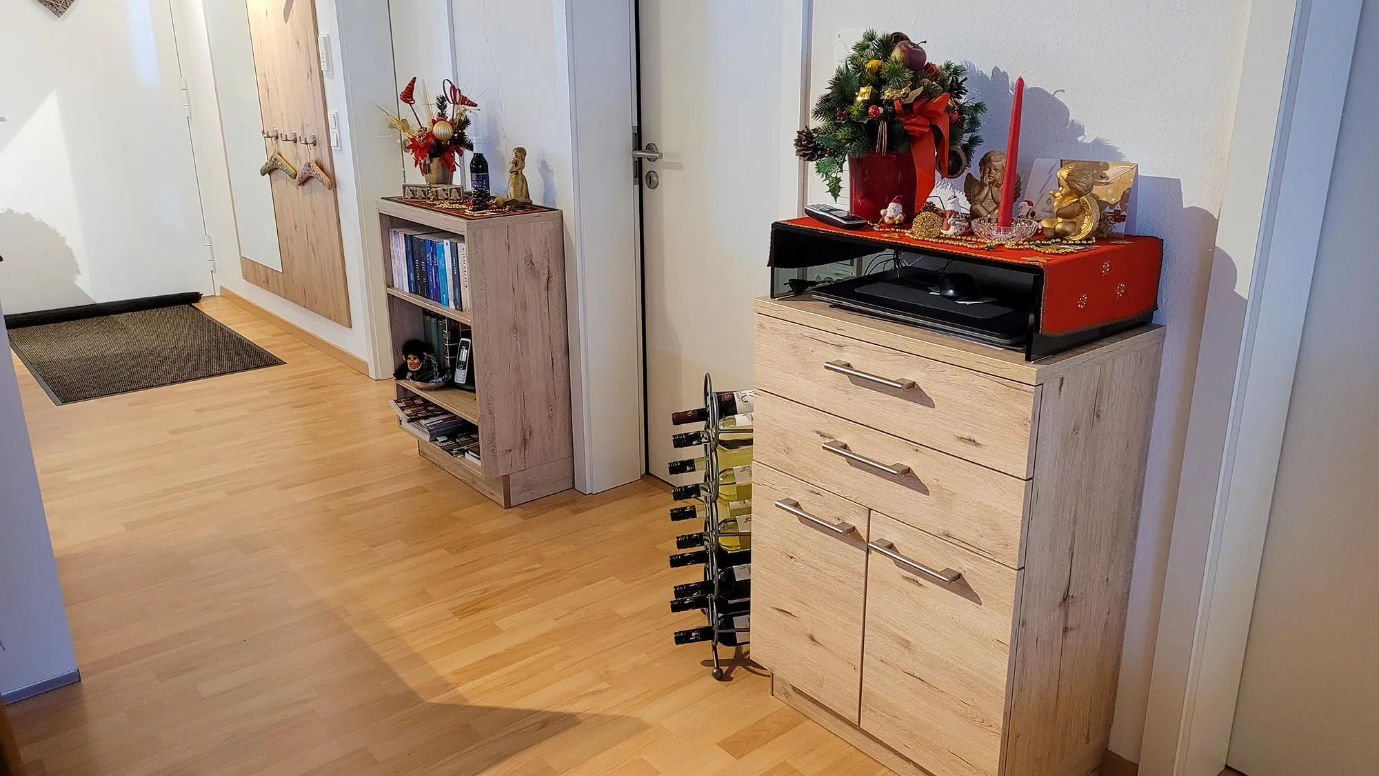 Diele mit Sideboard und Hochkommode in Eiche-Holzoptik, davor freistehendes Weinregal, Hochkommode mit weihnachtlicher Dekoration