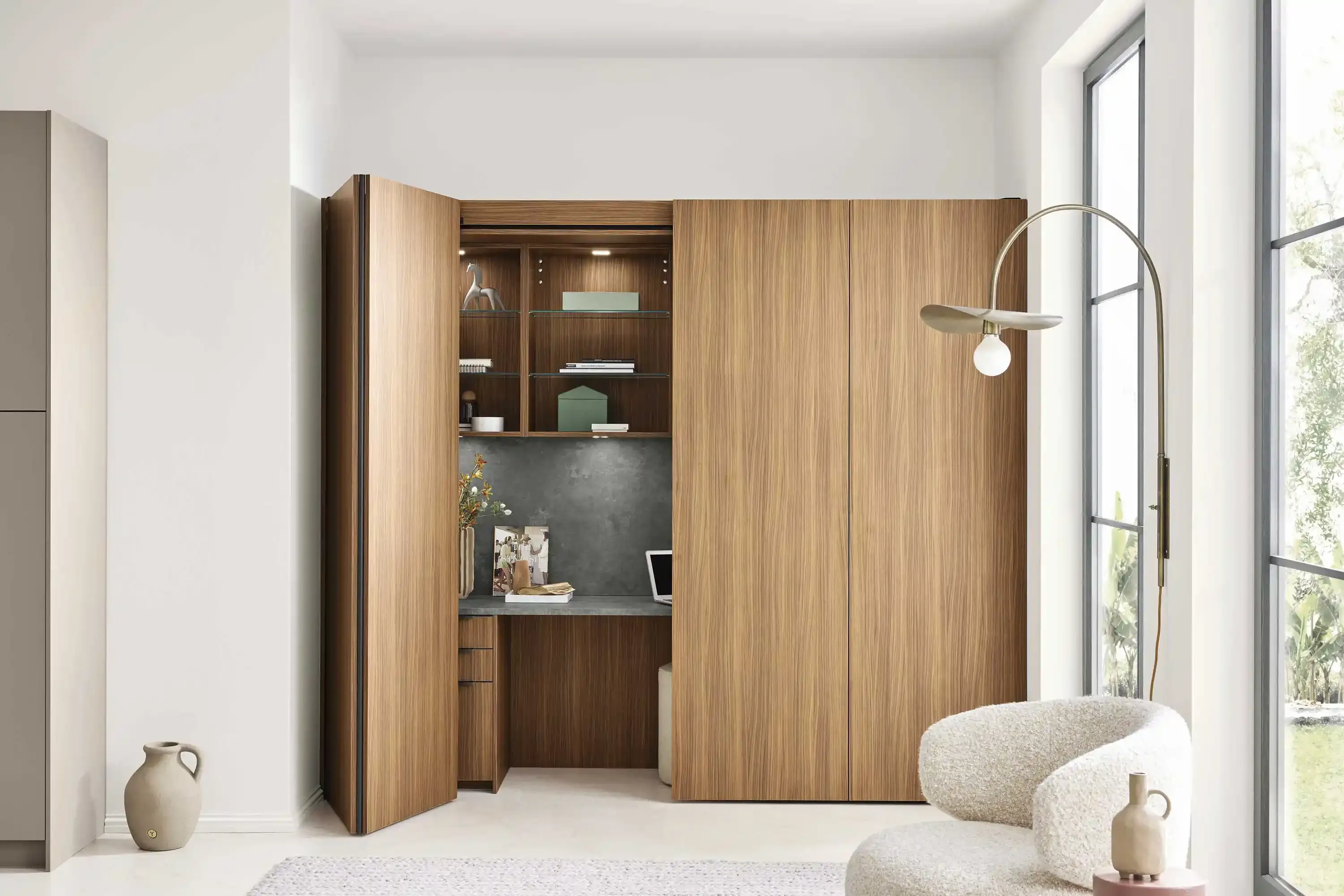 Geöffneter Pocket-Door-Schrank in Nussbaum mit integriertem Home-Office und Bouclé-Sessel davor
