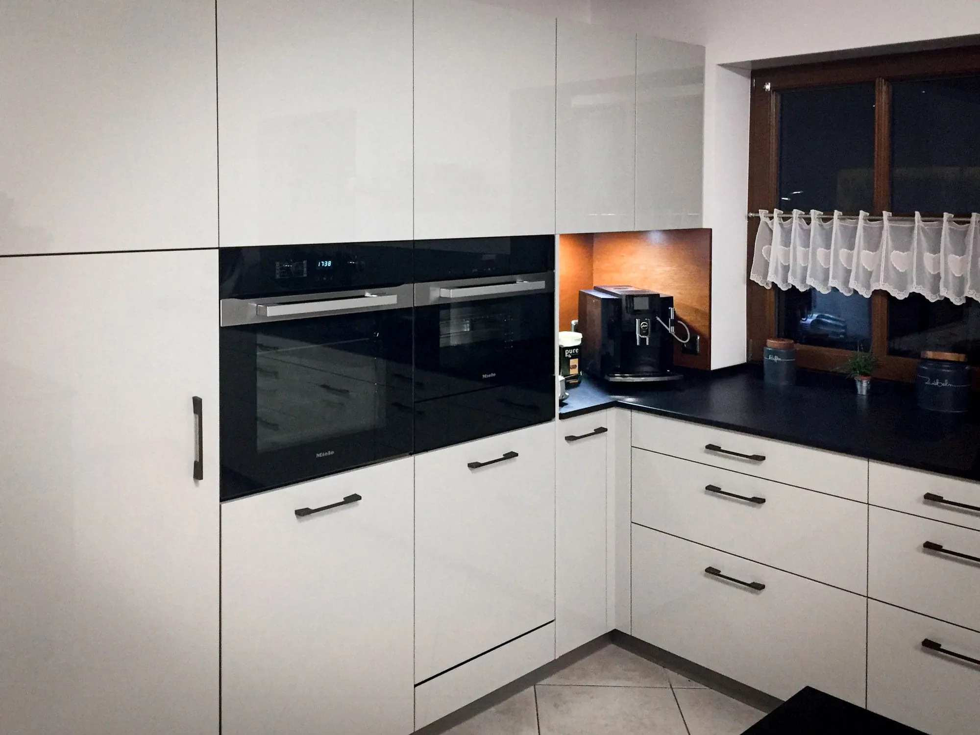 Eckküche mit Hochglanzfronten in Creme, Miele-Backofen, dunkler Arbeitsplatte und Holz-Nischenrückwand
