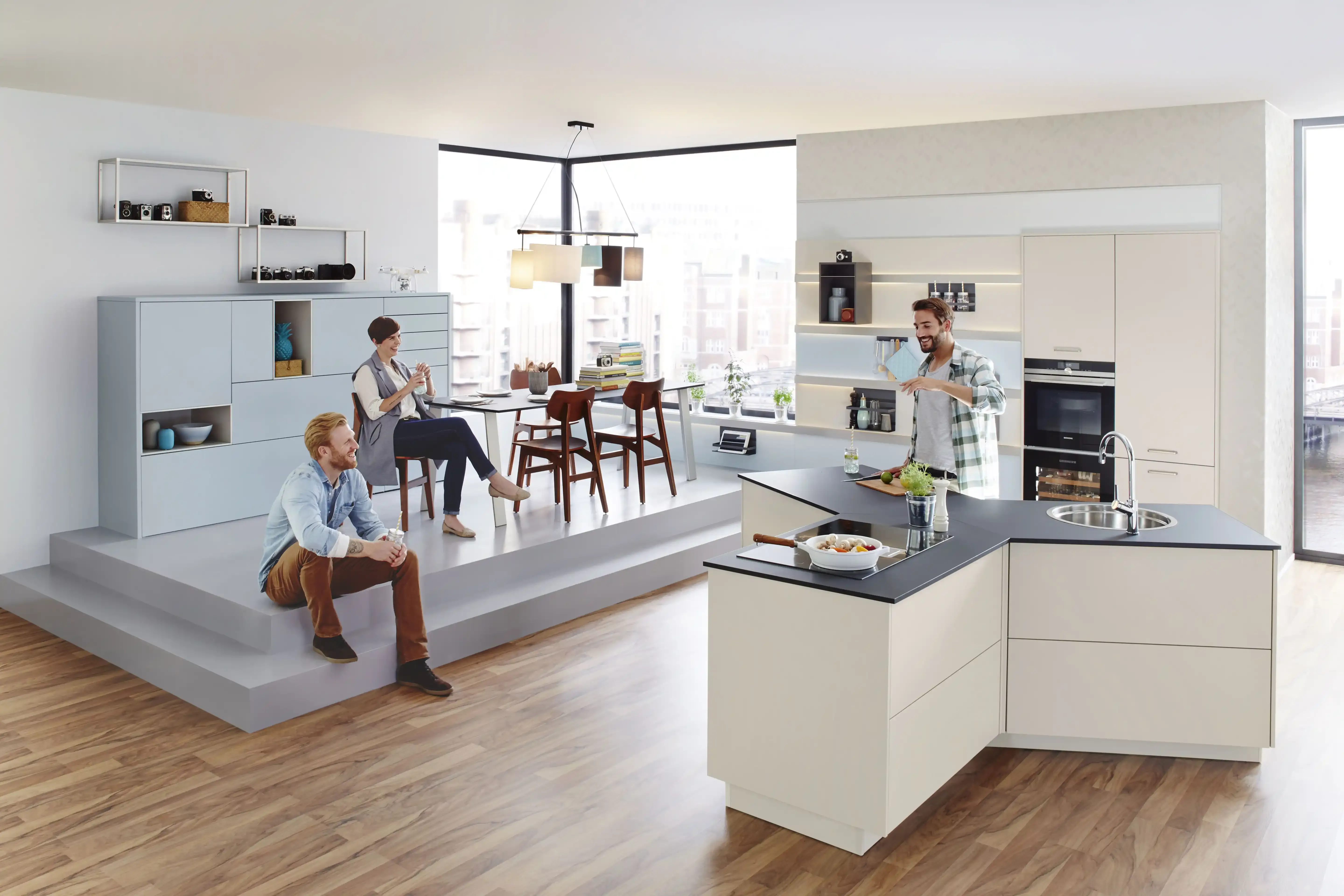 Lebensszene in offener Wohnküche mit Y-Insel, erhöhtem Bar-Plateau und vier Personen beim Plaudern und Kochen