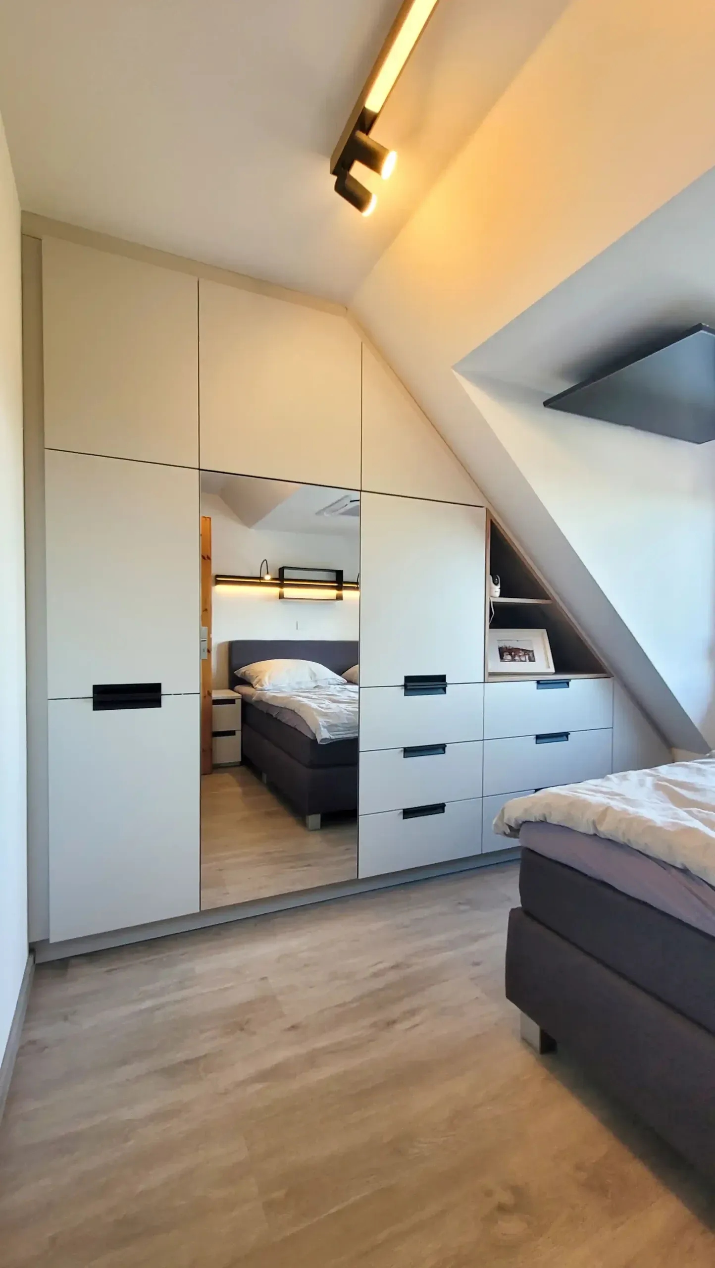 Dachgeschoss-Schlafzimmer mit Doppelbett und vollständig in die Dachschräge eingebauter Schrankwand.