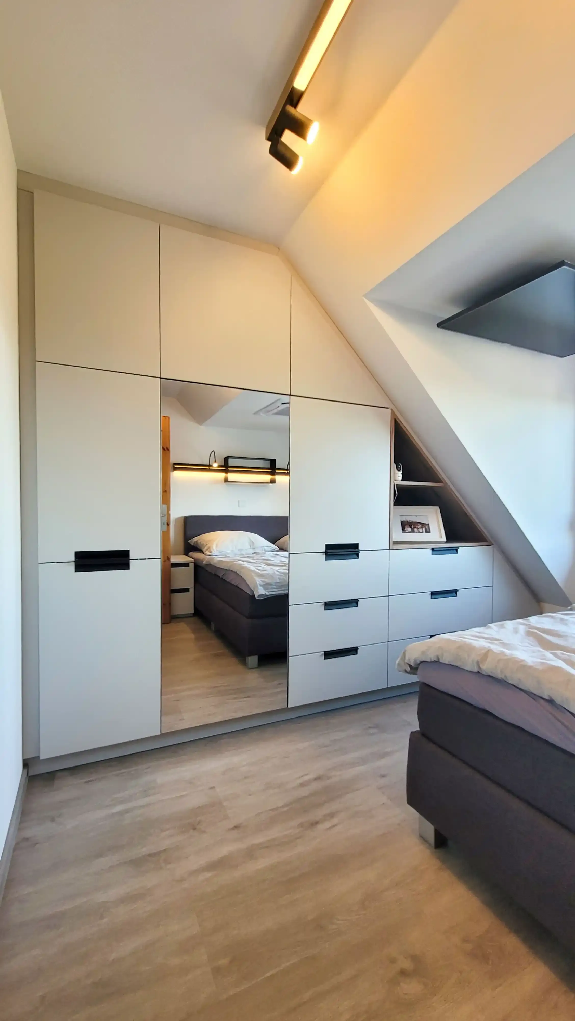 Dachgeschoss-Schlafzimmer mit Doppelbett und vollständig in die Dachschräge eingebauter Schrankwand.