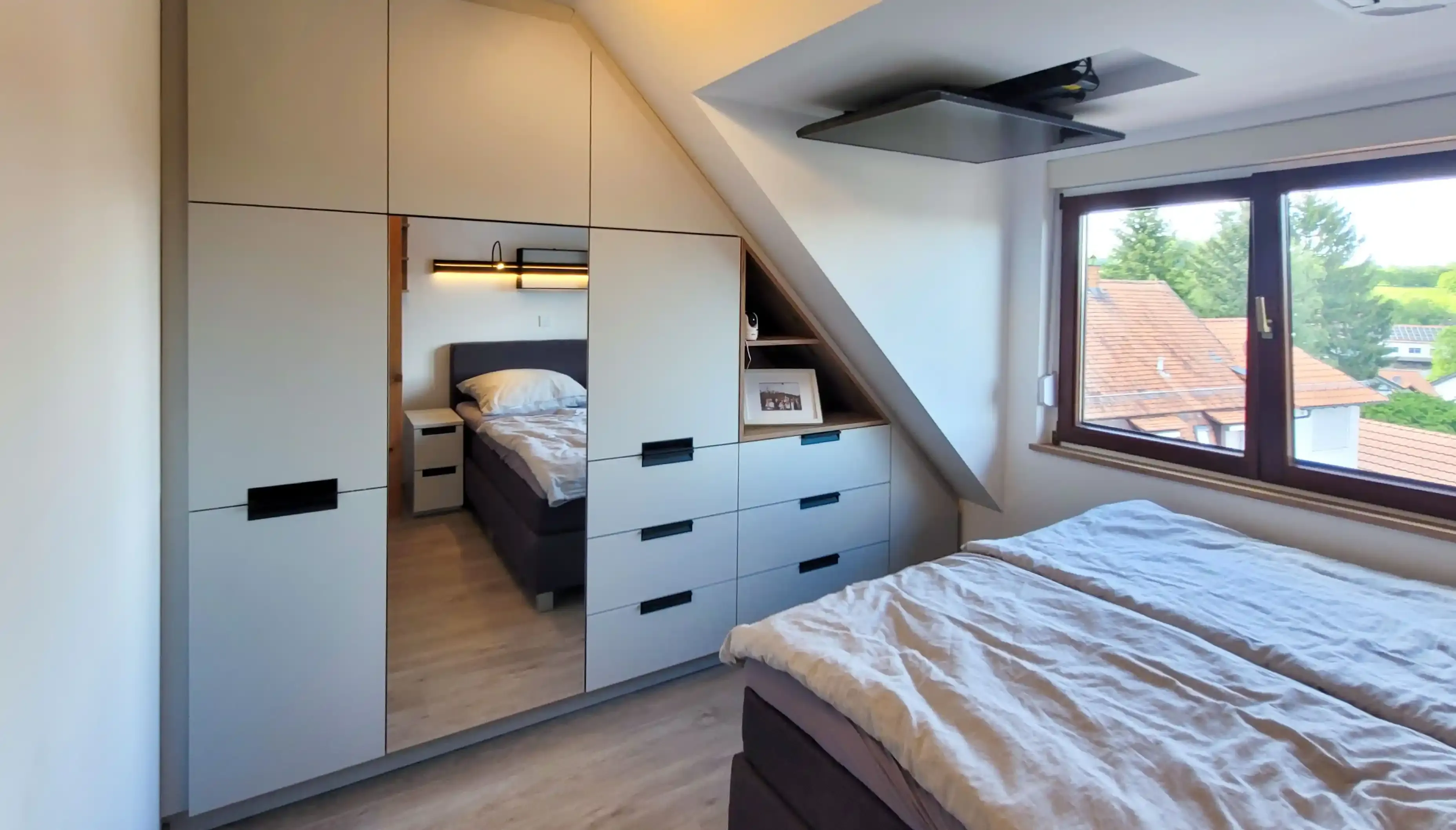 Dachgeschoss-Schlafzimmer mit Doppelbett, maßgefertigter Einbauschrankwand und Spiegelelementen.