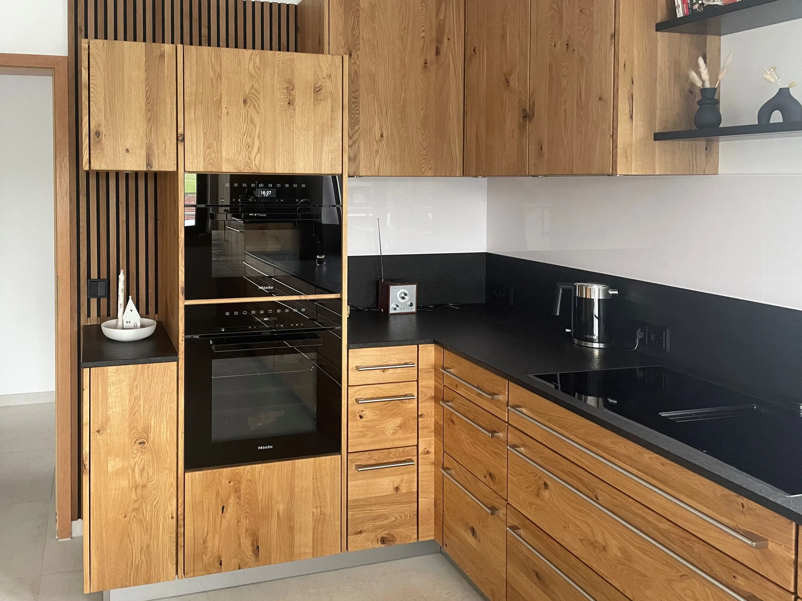 Eichenholz-K-Küche mit Backofen, schwarzer Arbeitsplatte, Holzlamellen-Wand und Wandregal