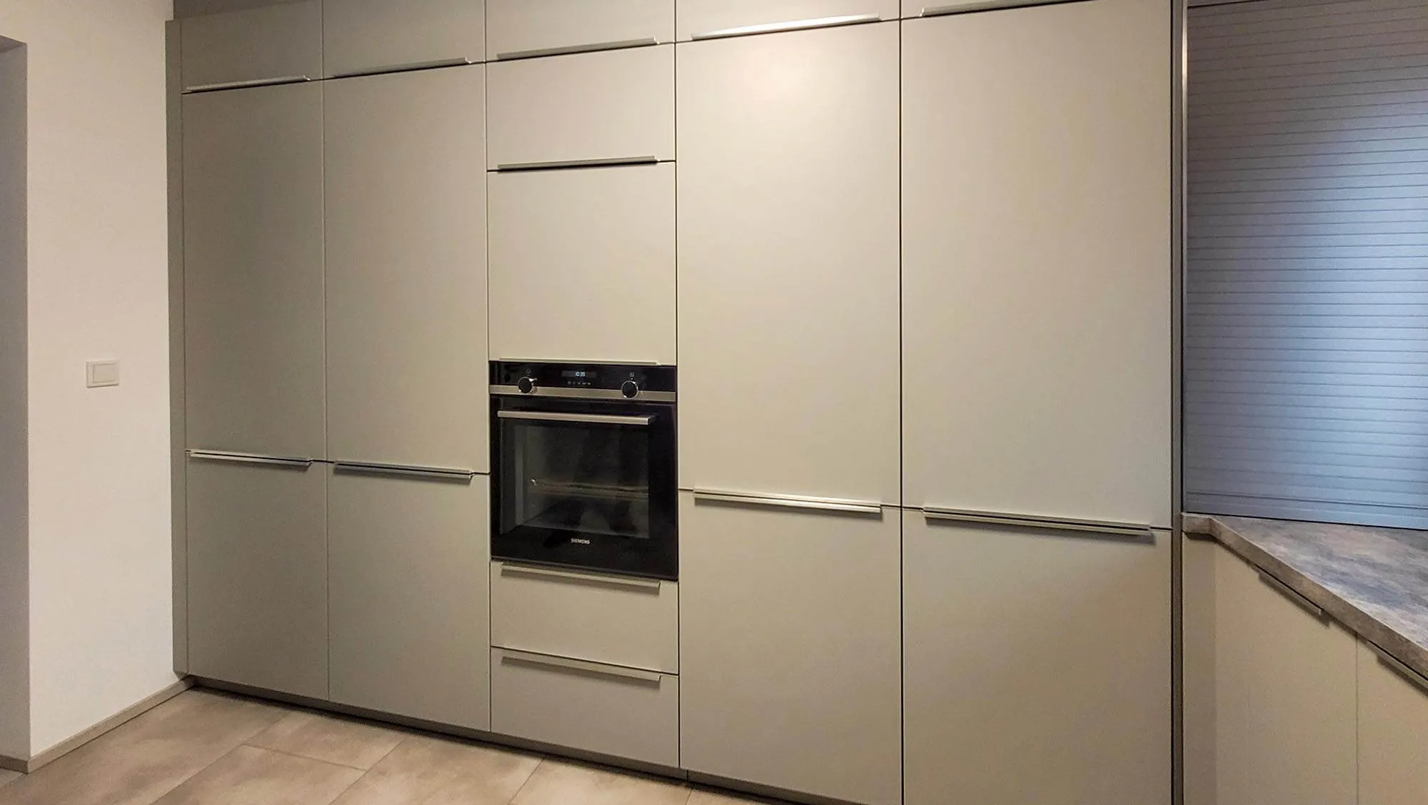Beige Hochschrankwand mit eingebautem Backofen, grifflose Fronten, rechts angeschnitten ein Eckbereich der Arbeitsplatte