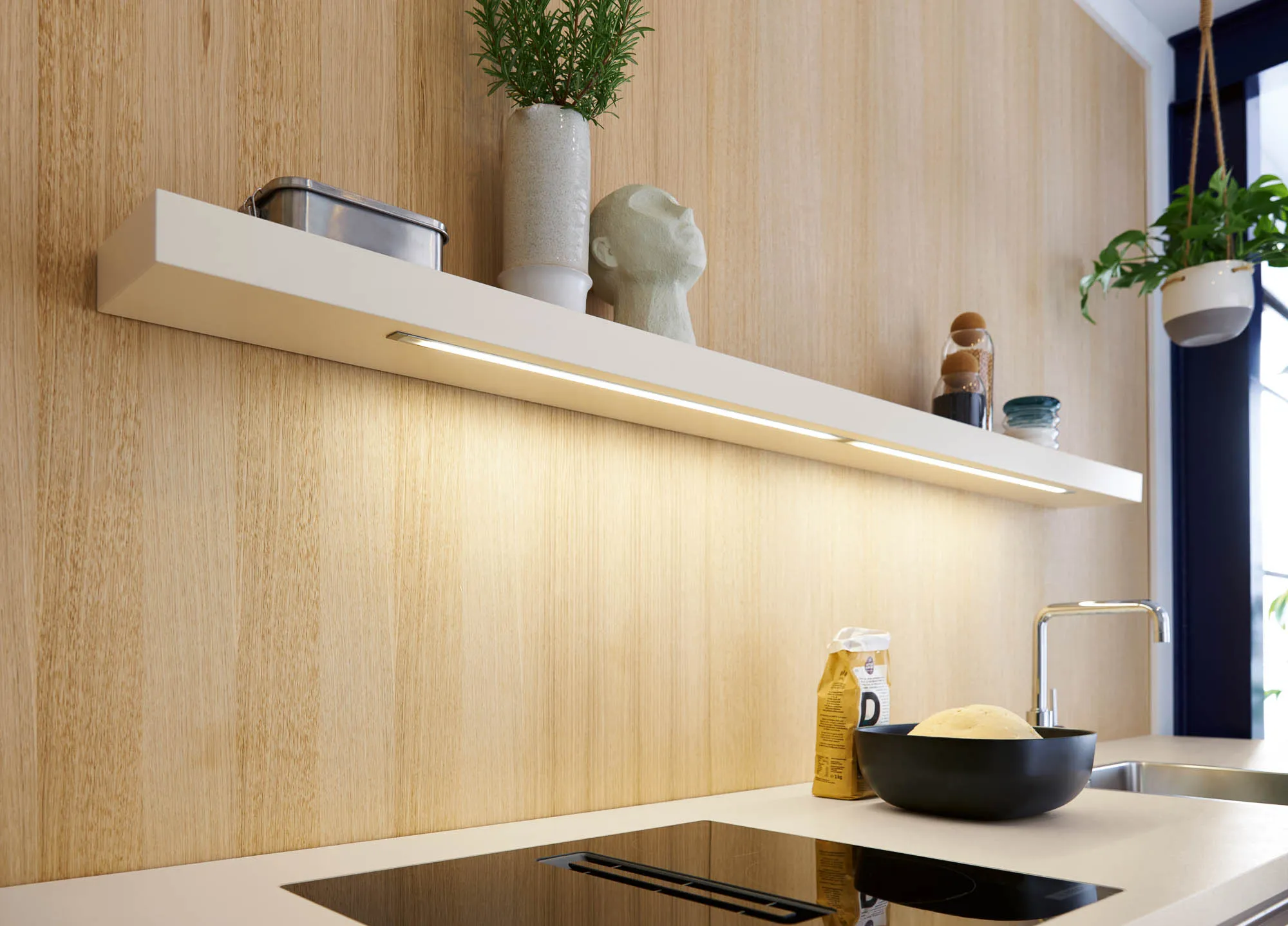 Beleuchtetes Wandbord in Muschelweiß matt mit integrierter LED-Leuchte vor Holzwand, dekoriert mit Vorratsgläsern, Vase und Skulptur über Kochfeld