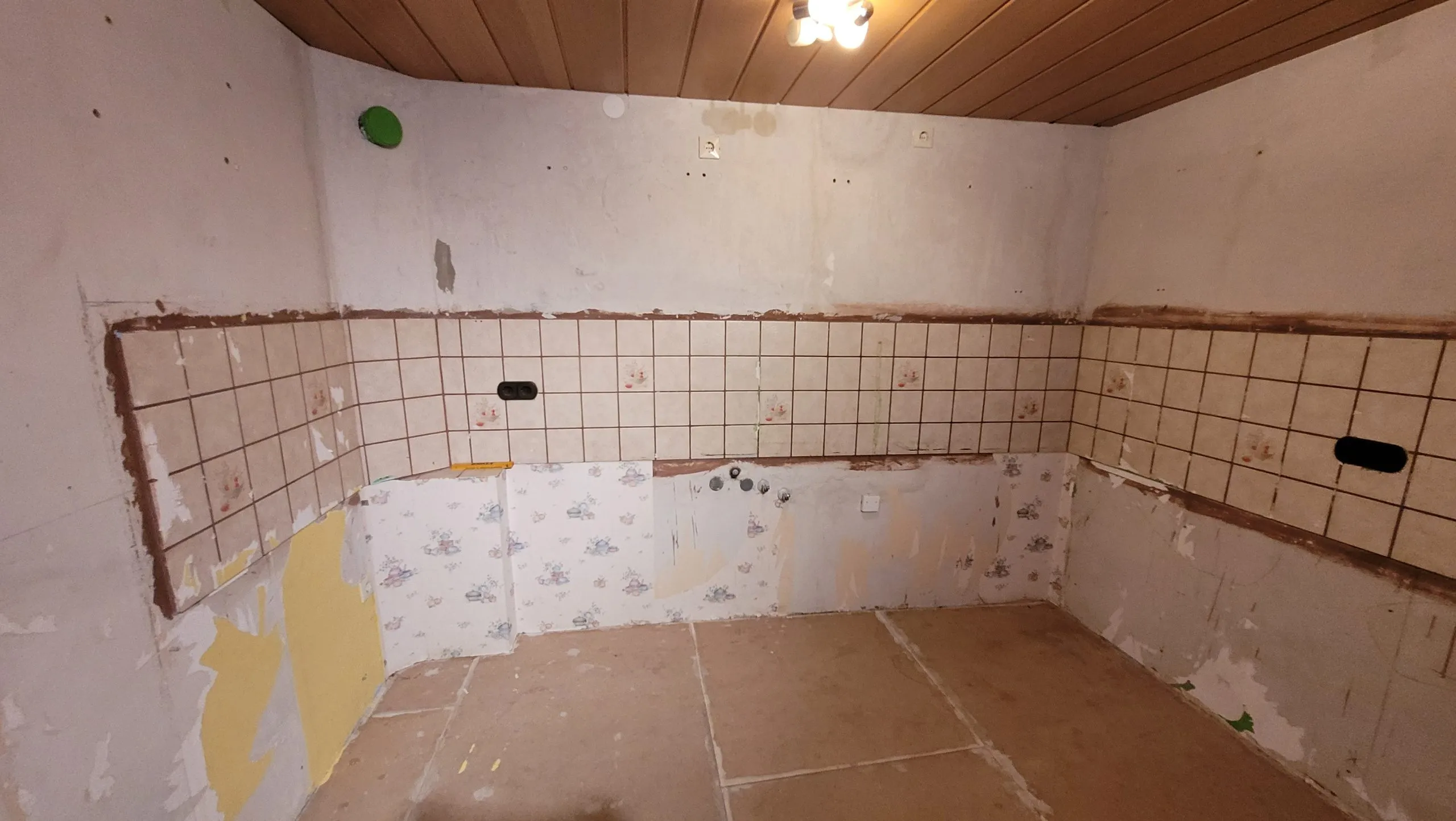 Leerer Küchenraum vor der Renovierung mit alten Wandfliesen und diagonal abgestellter Raumecke