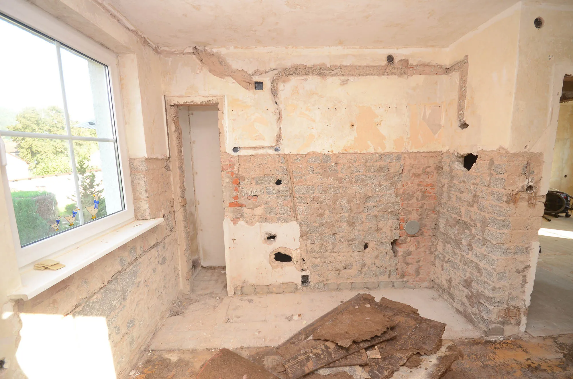 Unsanierter Küchenraum mit freigelegter Ziegelwand, Fensternische und Bauschutt vor dem Umbau