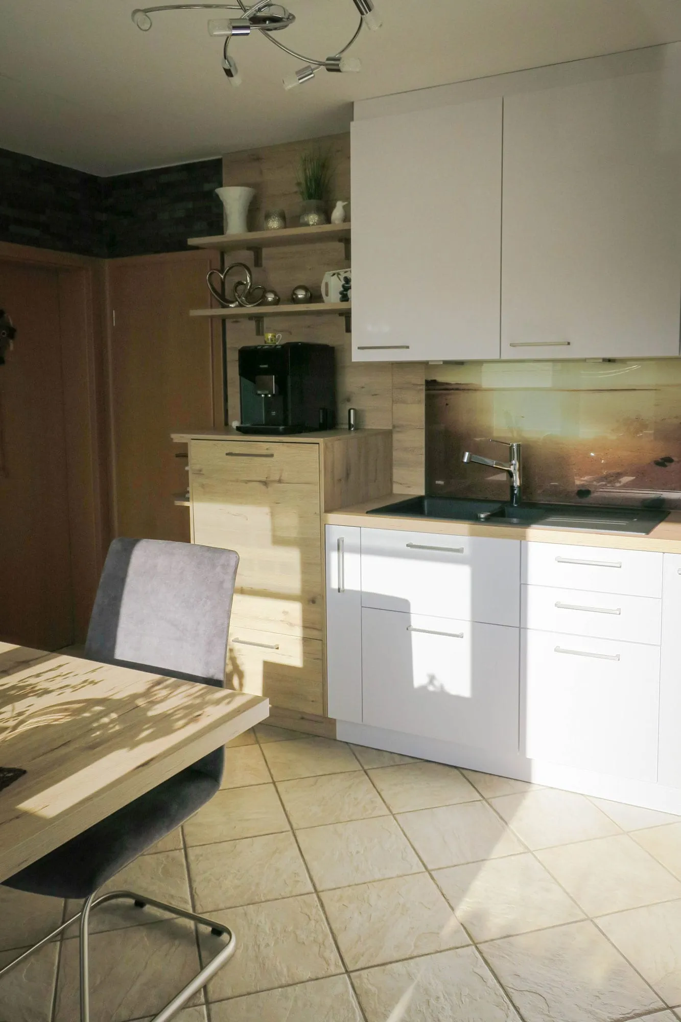 L-Küche mit Spülbereich und Sonnenuntergang-Spritzschutz, Eckschrank in Eiche-Holzoptik mit Kaffeevollautomat und offenen Holzregalen, weißen Hängeschränken und Esstisch im Vordergrund