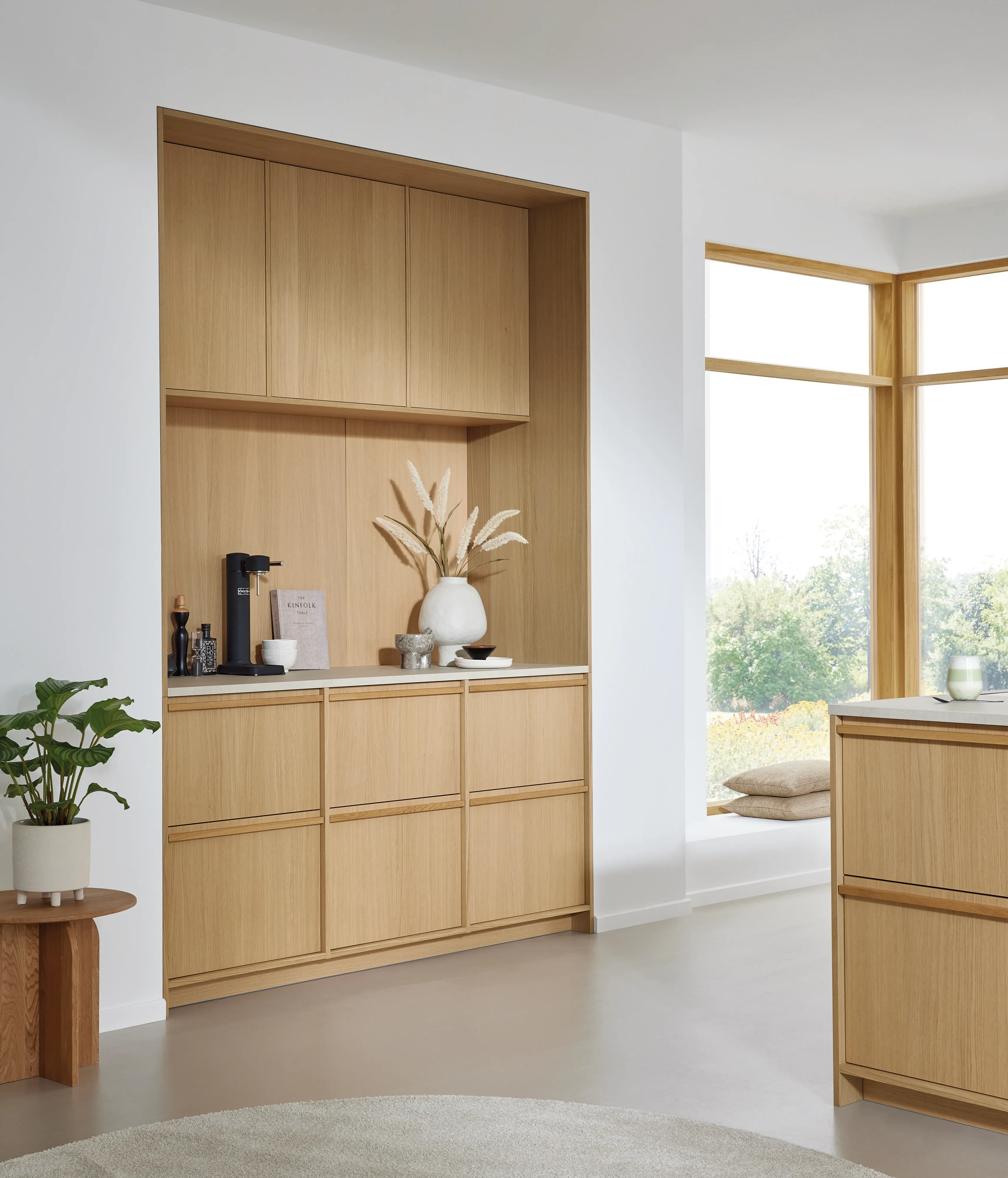 Wohnliche Nische in heller Eiche mit Kaffee-Station, Pampasgras-Vase und Fensterfront mit Sitzbank