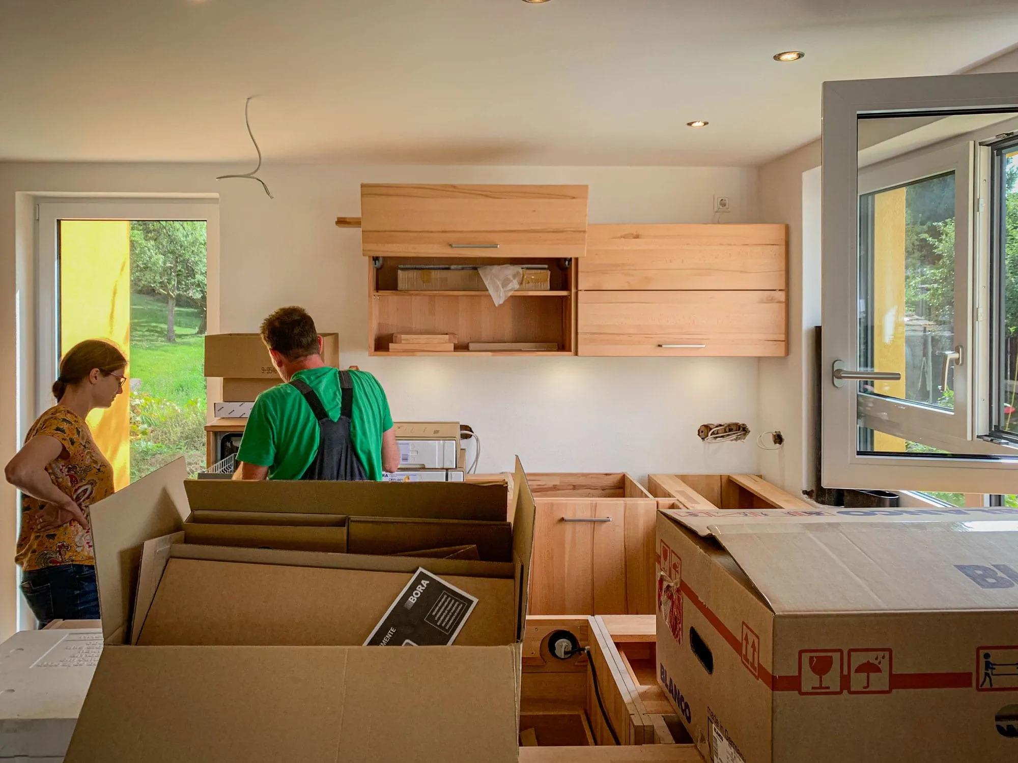 Aufbau-Aufnahme der Massivholz-Küche während der Montage mit Verpackungskartons und bereits montierten Hängeschränken.