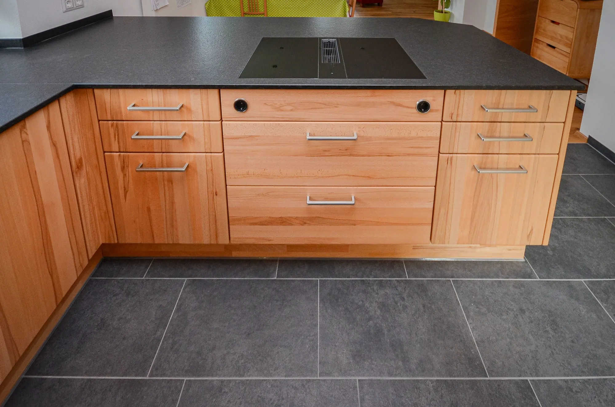 Detailaufnahme der Kochinsel einer Massivholz-Küche mit schwarzer Steinplatte und Induktionskochfeld mit integriertem Downdraft.