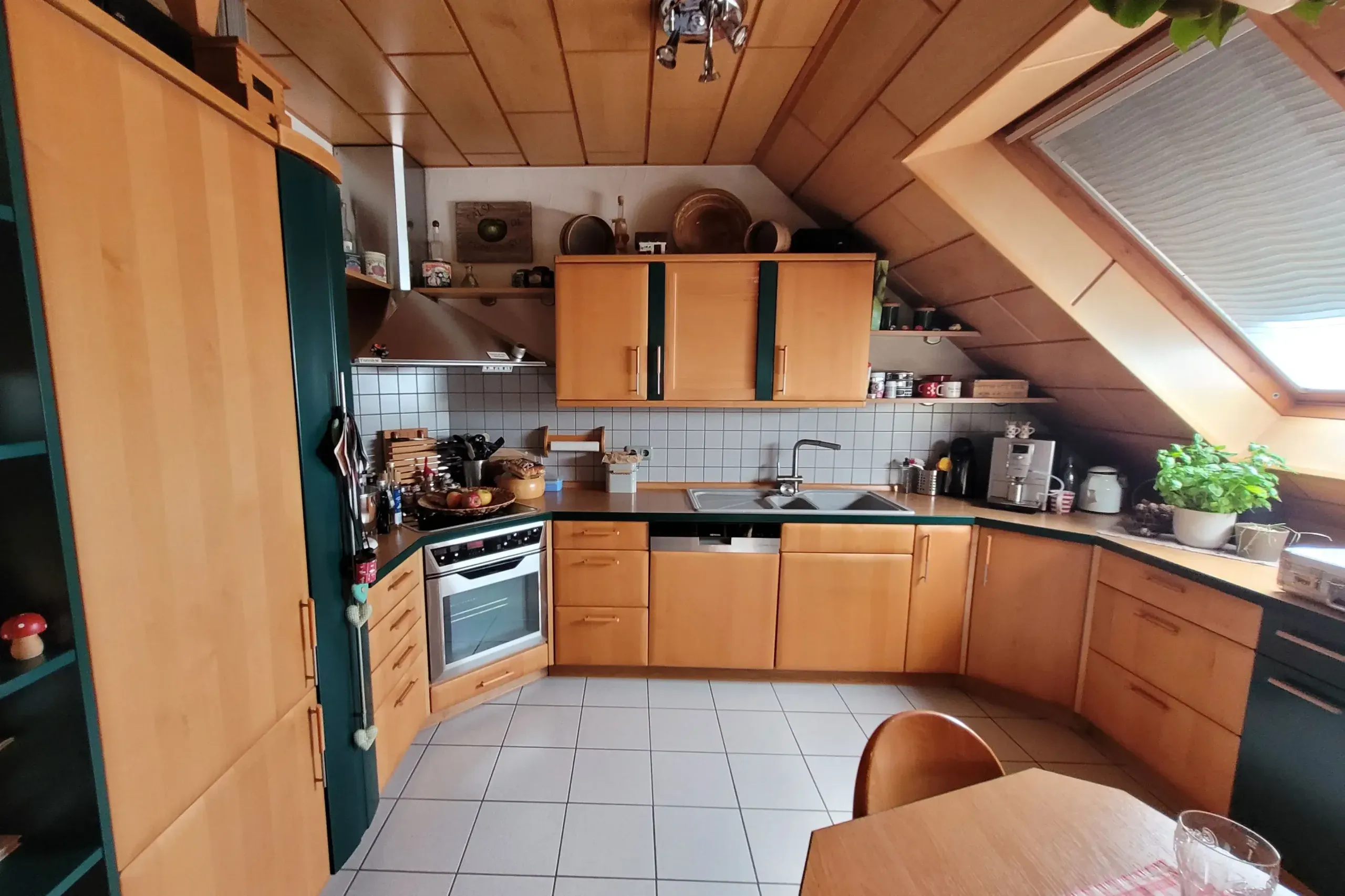 Vorher-Aufnahme der U-Küche aus weiterer Perspektive mit Backofen, Spüle und Holzdecken-Vertäfelung.