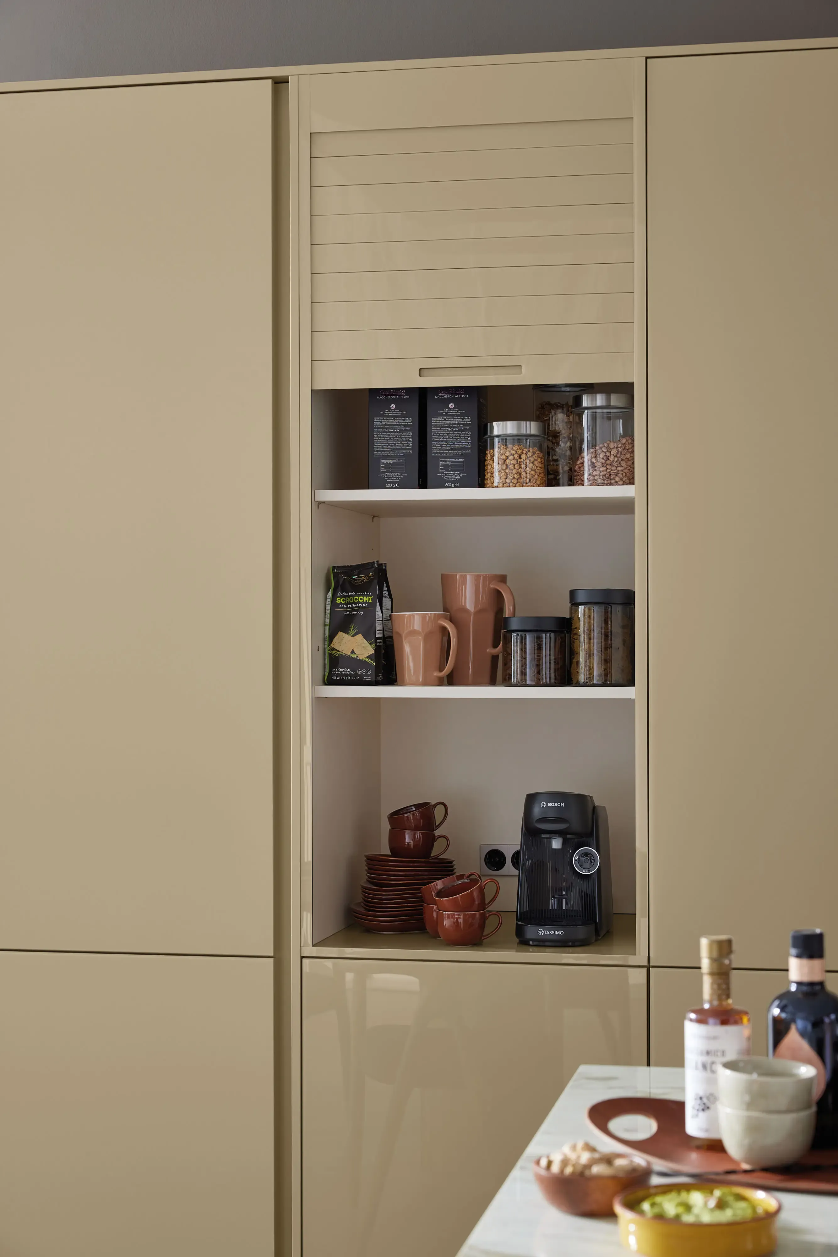 Geöffneter Jalousieschrank in Sandbeige mit Kaffeevollautomat, Vorratsdosen und Geschirr als Frühstücks-Station