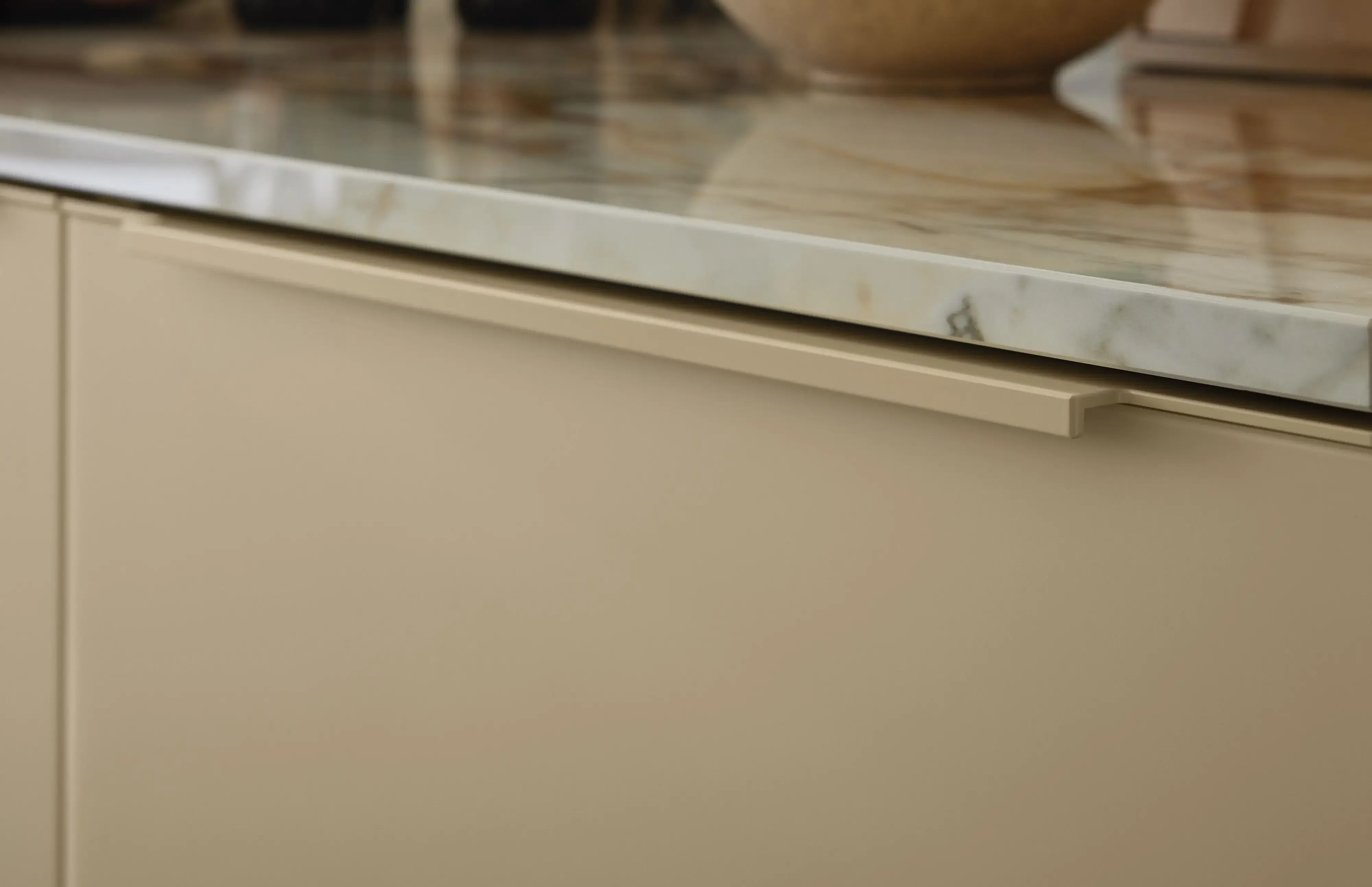 Materialnahaufnahme: grifflose Front in Sandbeige mit Marmor-Arbeitsplatte und Spiegelung der Tageslicht-Atmosphäre