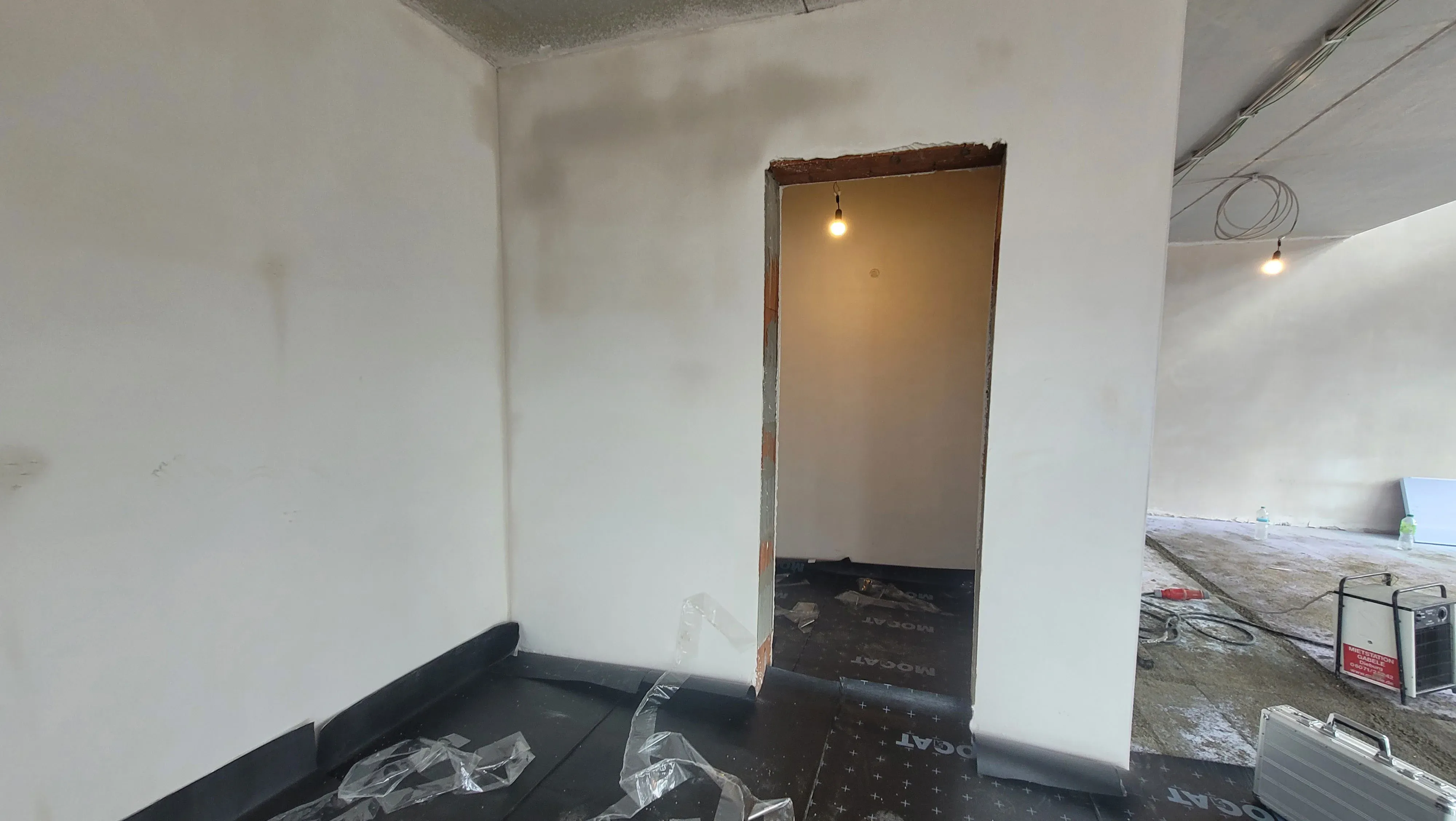 Vorher-Aufnahme im Rohbauzustand: leerer Raum mit Türöffnung, Bauschutz und losen Stromleitungen.