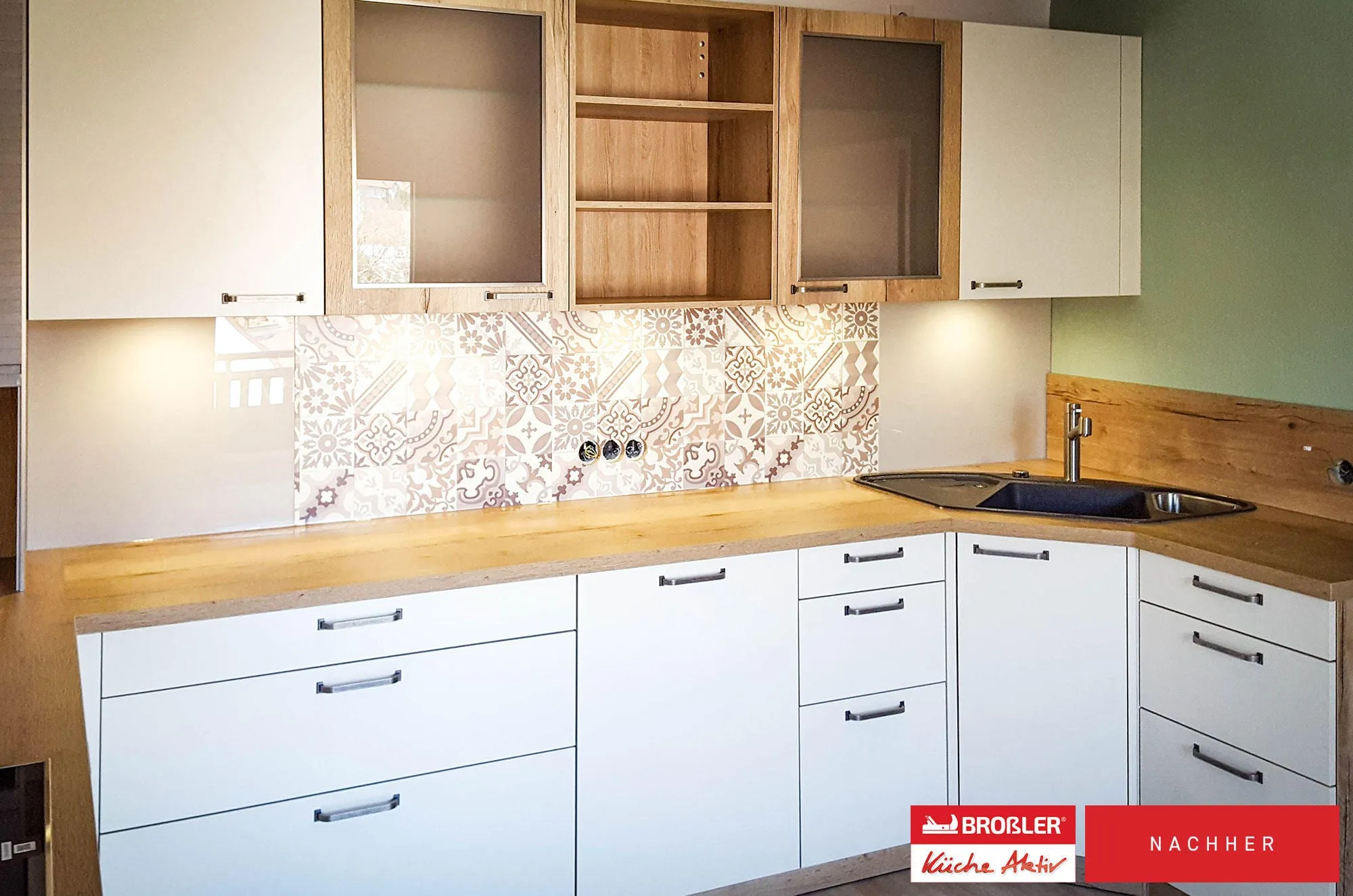Nachher-Aufnahme: Eckspüle in schwarzer Granitoptik in weißer L-Küche mit Mosaik-Fliesenspiegel und Massivholz-Arbeitsplatte.