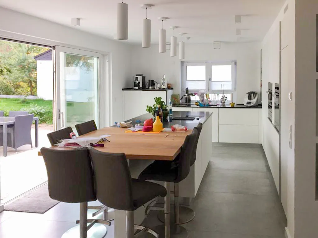 Offene Wohnküche mit Esstheke, großer Glasfront zum Garten und Stab-Pendelleuchten