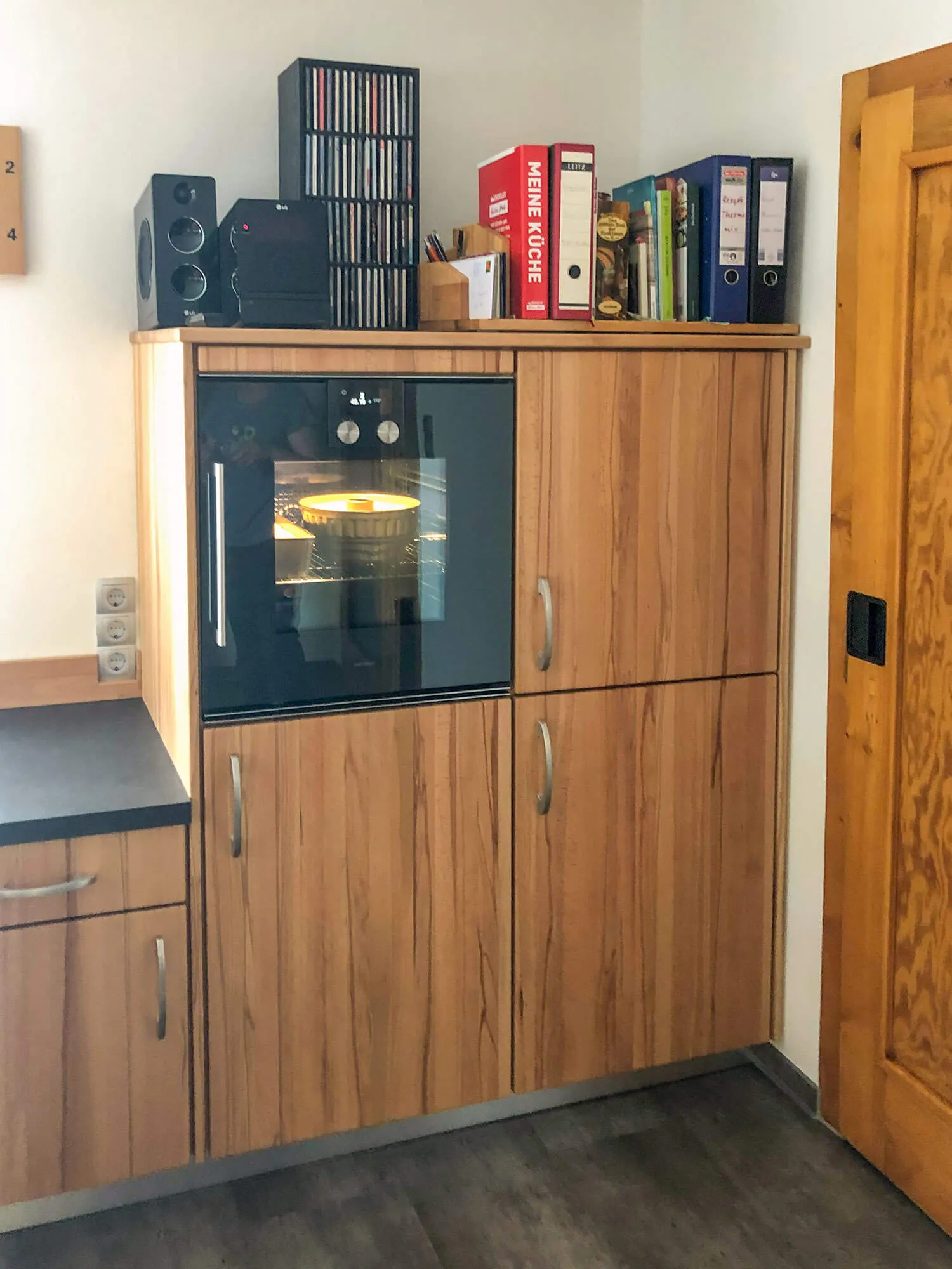 Hochschrankmodul mit eingebautem Backofen in Holzfurnier und Regalboard für Kochbücher und Audioanlage