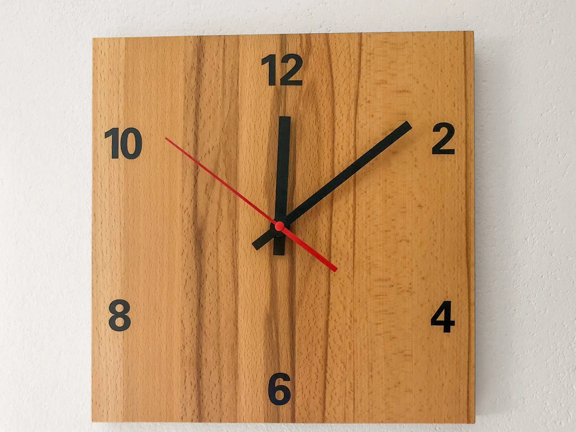Quadratische Wanduhr aus Buchenholz mit großen schwarzen Ziffern und roten Zeigern an heller Wand – Küchen-Deko-Detail