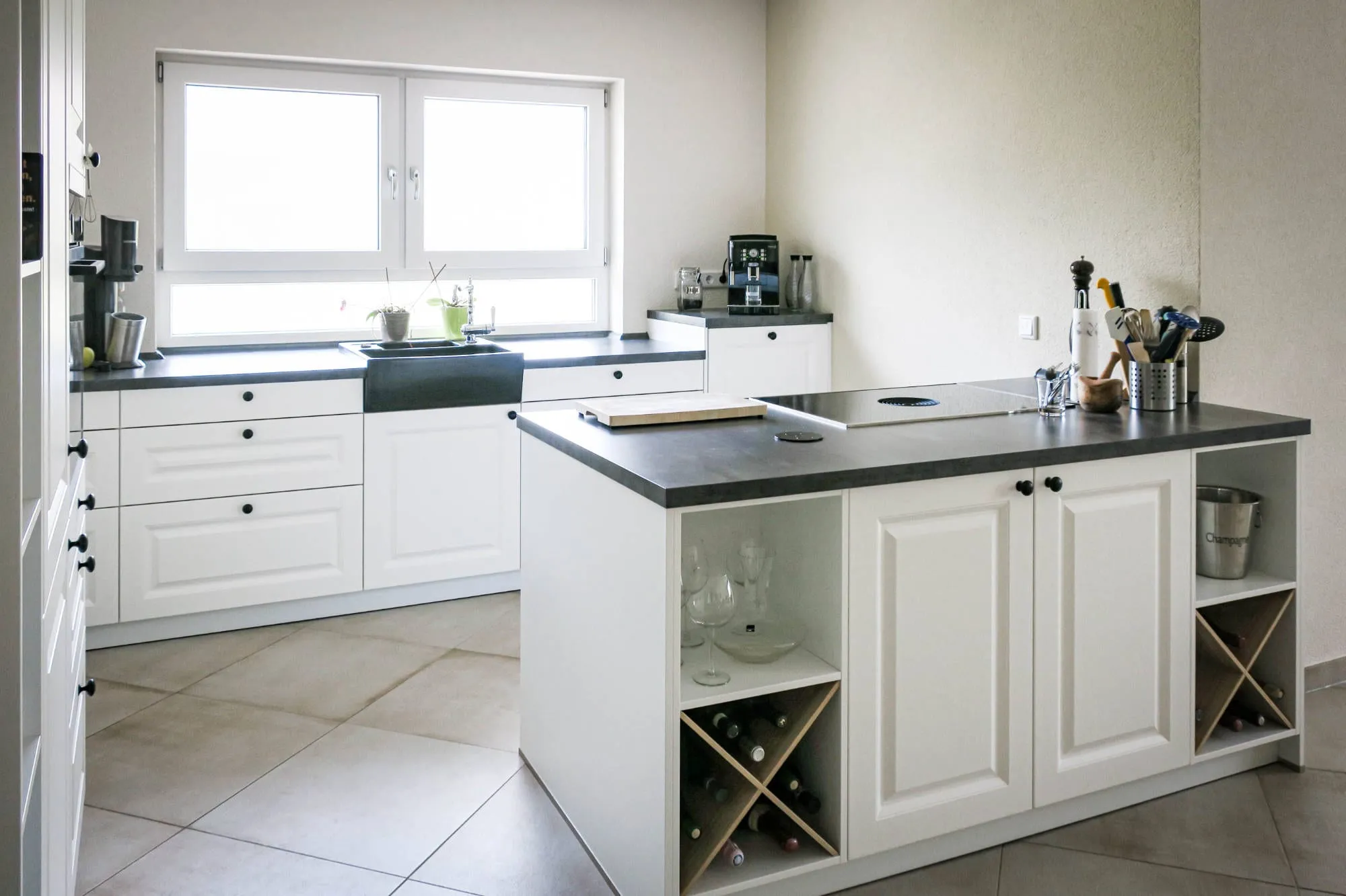 Landhaus-Kochinsel mit integriertem Holz-Weinregal in Rautenform und offenen Seitenfächern, im Hintergrund Spüle am Doppelfenster und anthrazitfarbene Arbeitsplatte