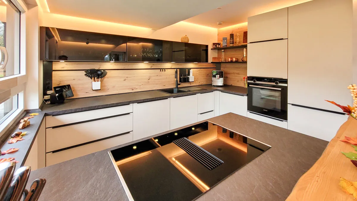 Gesamtansicht der U-Küche mit weißen Unterschränken, Kochinsel mit Muldenlüfter und dunklem Hochschrank mit Backofen.