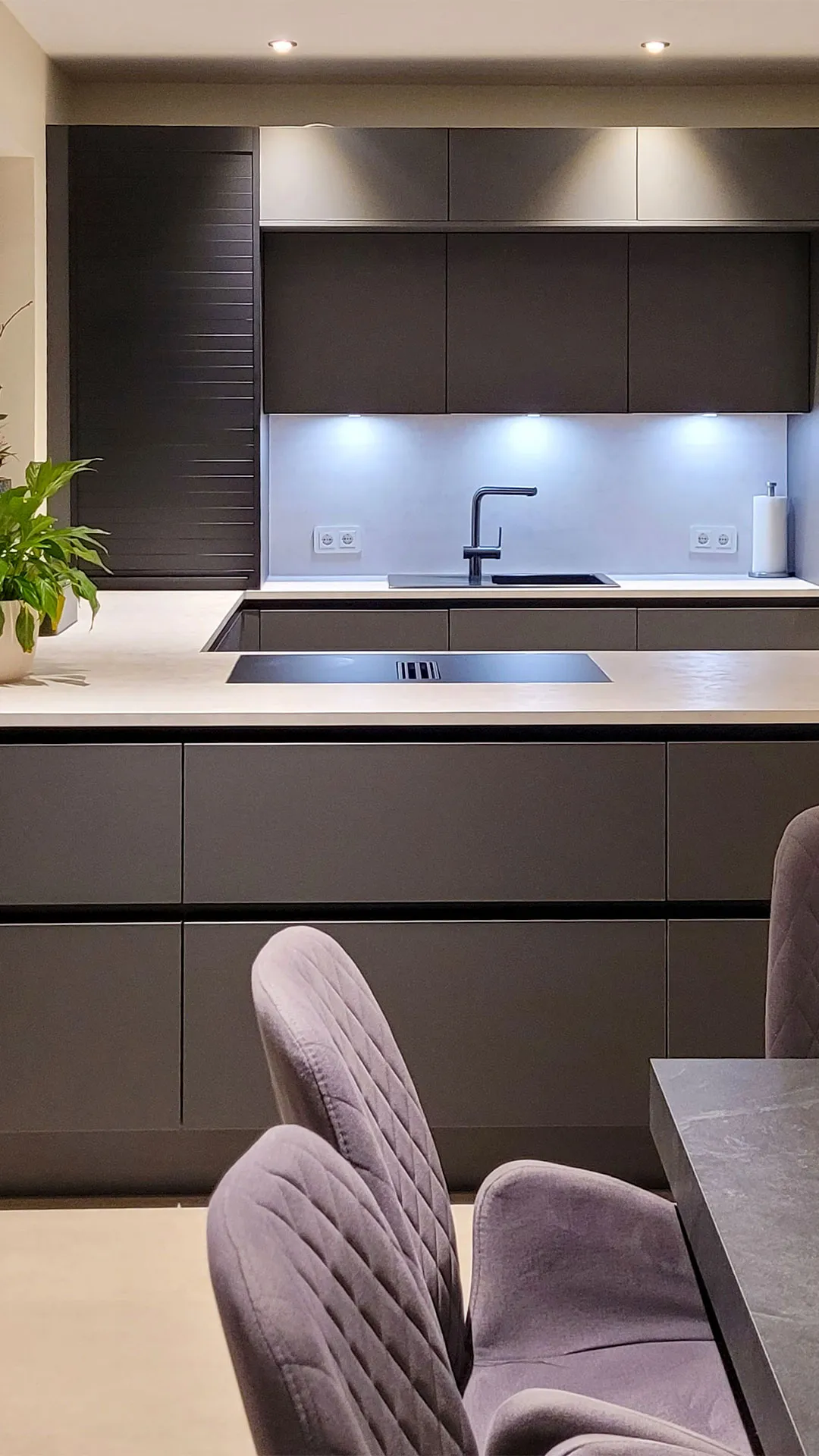 Moderne Anthrazit-Küche mit Lamellenfronten und heller Arbeitsplatte mit Edelstahl-Spüle, Blick aus dem Esszimmer.