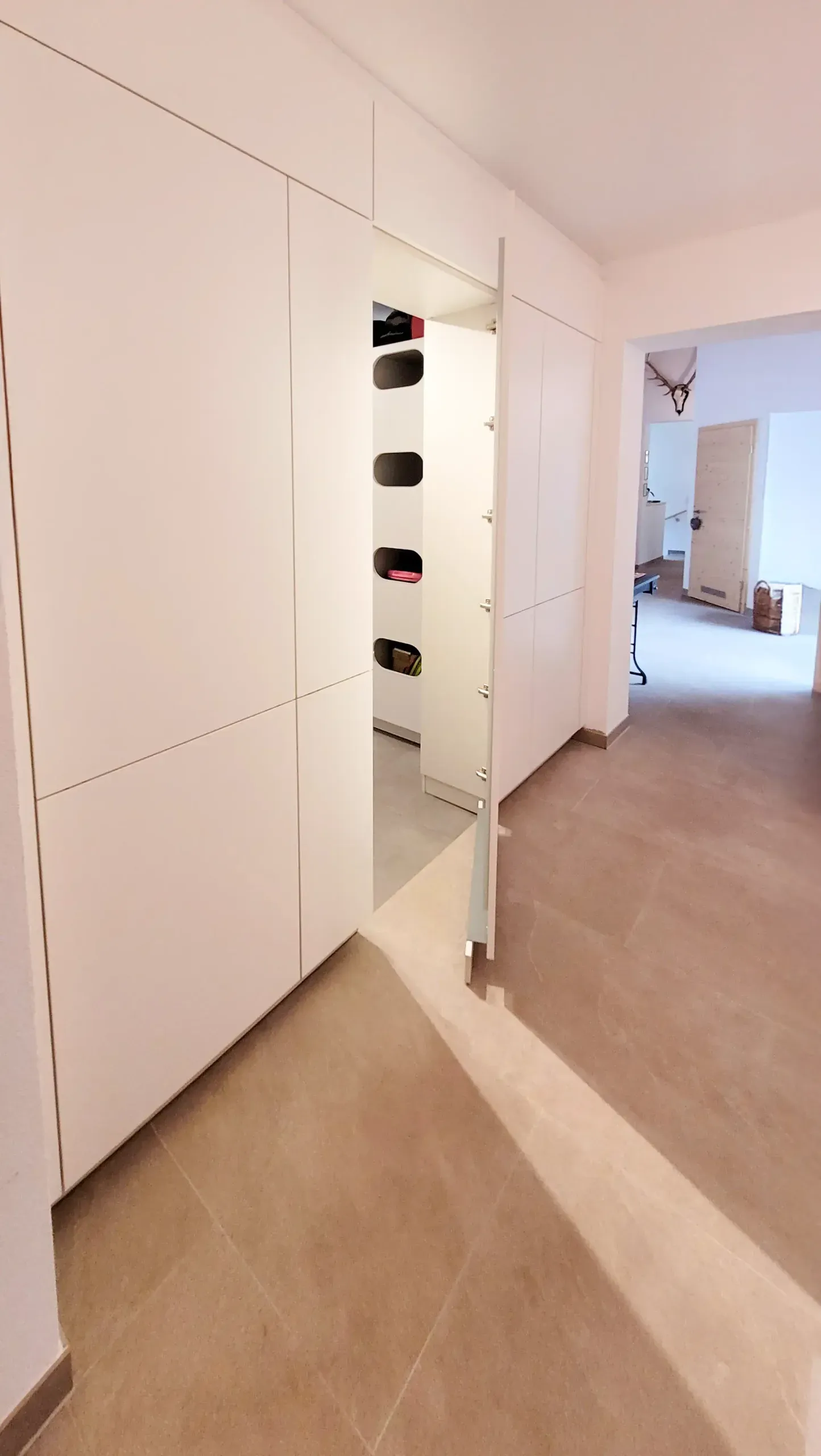 Hochschrank der Garderobe mit geöffneter Tür und runden Innennischen vor offenem Wohnraum.