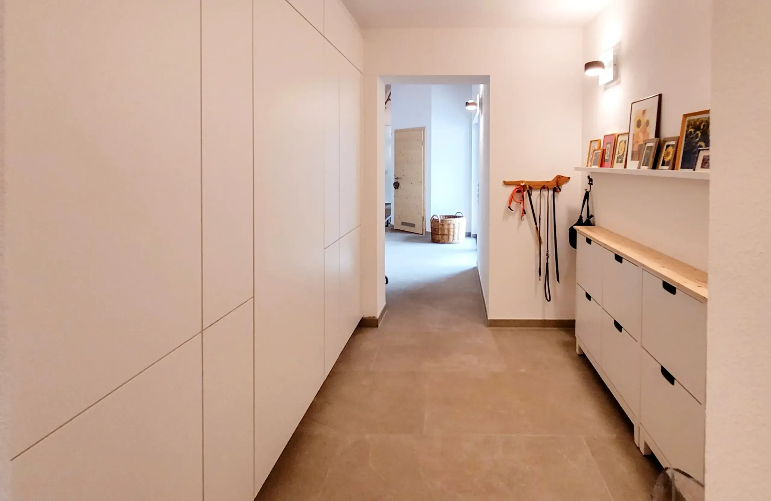 Einbau-Garderobe im Flur mit raumhoher weißer Schrankfront und Schuhschränken mit Holzablage.