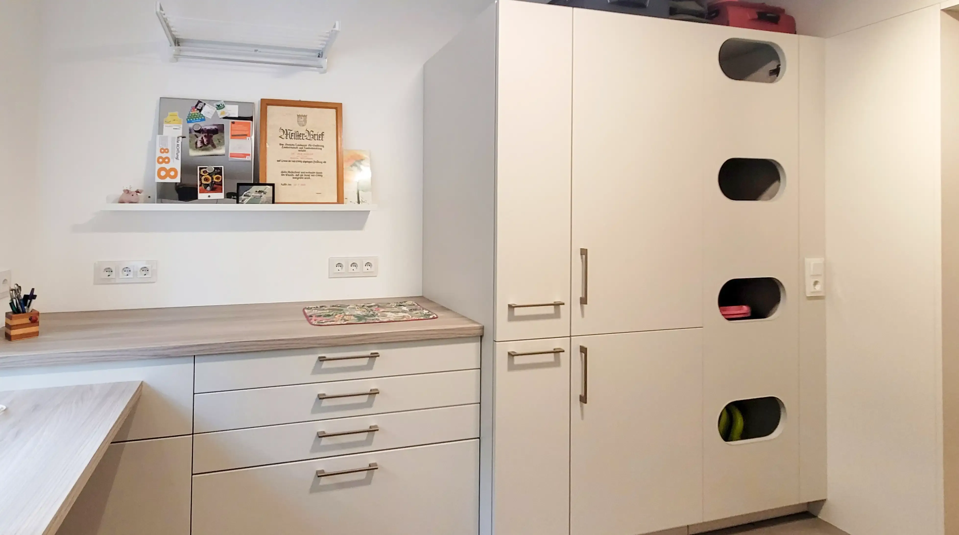 Hauswirtschaftsraum mit integriertem Arbeitsplatz und weißer Schrankwand mit runden Sichtfenstern.