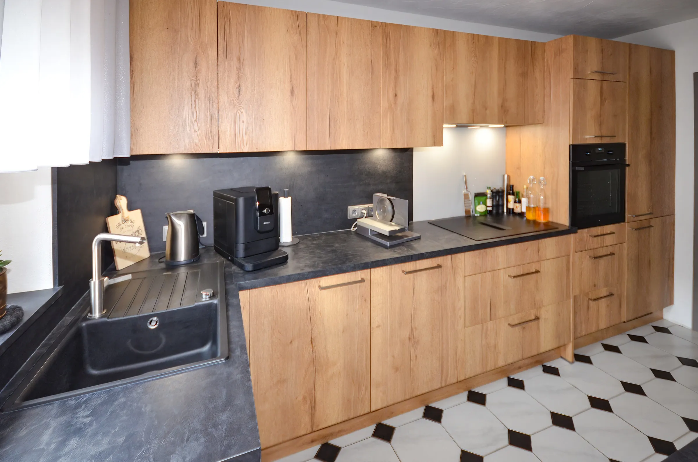 Spülbereich der renovierten Küche mit Holzfronten, schwarzer Spüle und dunkler Rückwand