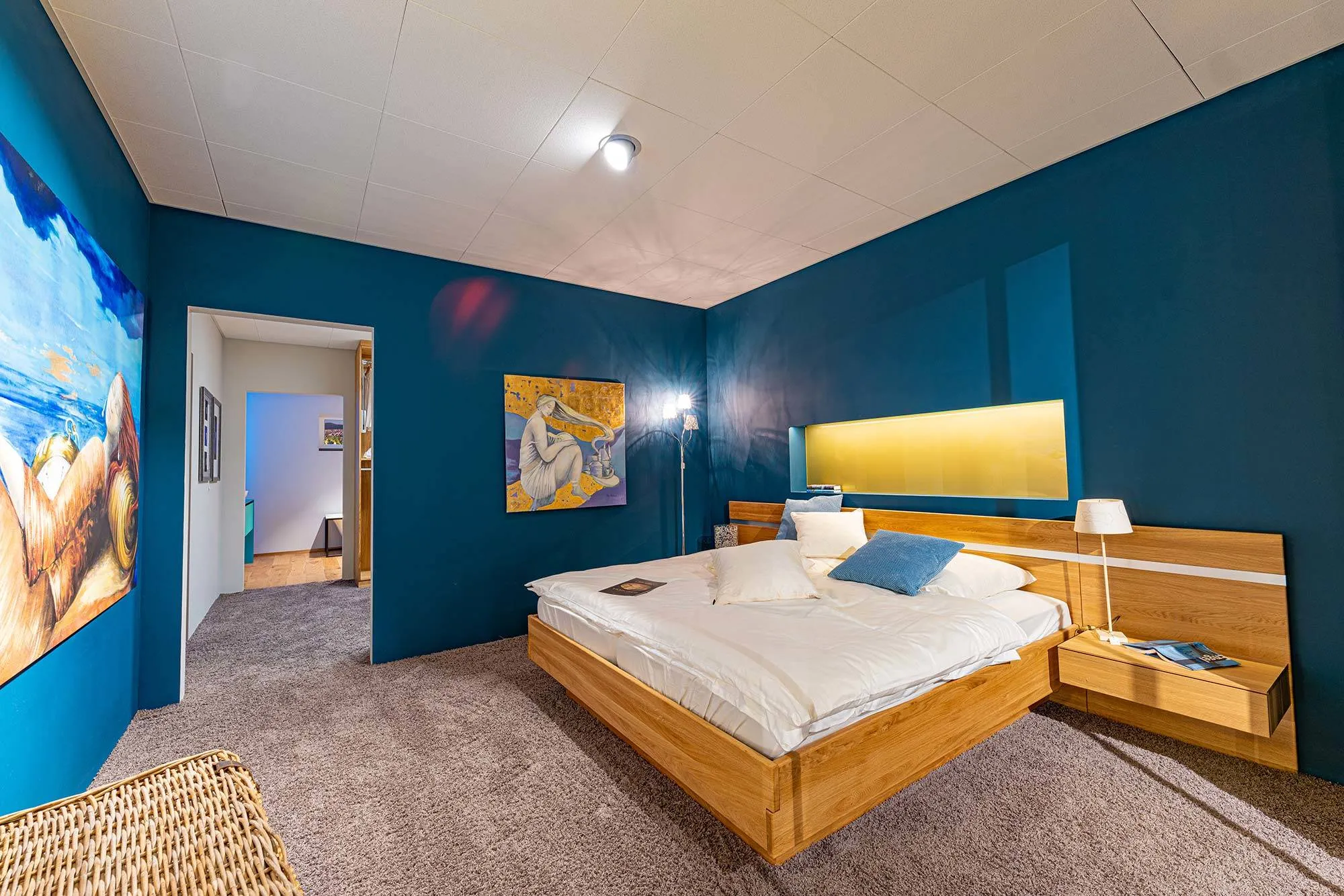 Haus im Haus – Schlafzimmer mit dunkelblauer Akzentwand, Doppelbett und warmem Holzboden in der Broßler Hausausstellung